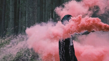 A mysterious man in a raincoat with a smoke bomb in his hand. The witch smokes in the forest with magical pink smoke. Mystical background. - Powered by Adobe