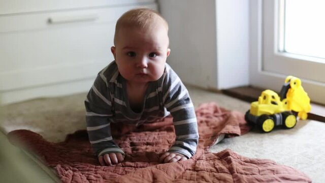 Cute Caucasian baby learns to crawl and play on the floor at home, bangs his palm on the glass, baby 5 6 months on his stomach on the floor, the development and safety of children,