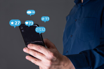 A man's hand holds a phone, icons of messages from social networks.