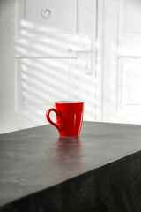 Red mug on table and white dooors with shadows. 
