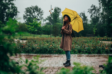 Obraz premium Beautiful young woman holding a yellow umbrella while walking in the park