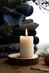 Burning candle on a wooden table near the window. Vertical image.