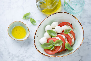 Green bowl with italian caprese salad over light-grey marble background, high angle view, horizontal shot