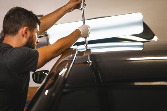 Close shot of a mechanic in protective gloves in process of removing dents from the roof of the car at the service station.