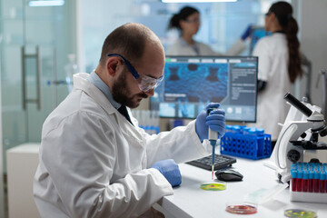 Scientist biologist man putting chemical fluid in petri dish using medical micropippete analyzing...