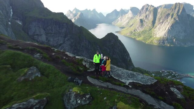 Happy family on top of the mountains and looking down on Reine after climbing Reinebringen treeking path with lots of stairs, Lofoten, northern Norway