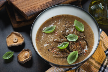 Bowl of soup made of porcini and shiitake mushrooms with addition of quinoa, studio shot on a dark brown metal background