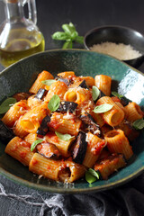 Pasta alla norma - Italian pasta with eggplante, tomato sauce and parmesan cheese on dark table. Top view. Healthy food.