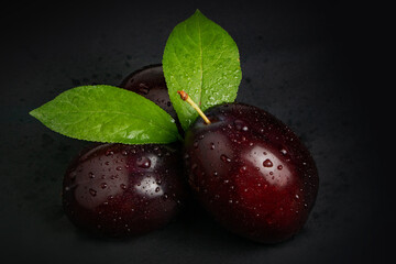 Plums with plum leaves and water drops on a dark background.