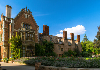 Facade of historical bricked building with a garden and tall chimney stacks at Cambridge England