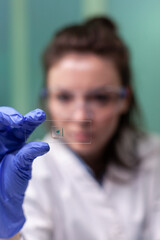 Portrait of botanist researcher woman holding microscope slide with green leaf sample discovering genetically modified plants during biological experiment. Chemist working in biochemistry laboratory