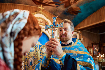 a priest blesses a young woman in a headscarf in an Orthodox church after a festive church mass
