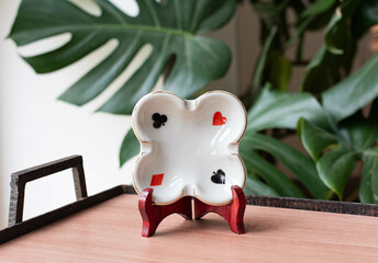 Vintage porcelain ashtray with poker signs on a wooden table with philodondendron in the background