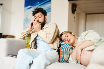 Man talking on cellphone while his pregnant wife sleeping on couch