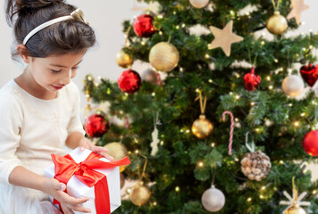 winter holidays, childhood and people concept - smiling little girl with gift box over christmas tree on background