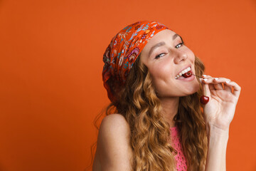 Young ginger woman in bandana smiling while eating cherry