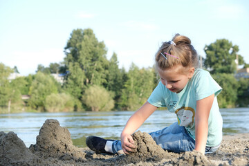 Child girl plays  with toys on the beach. Autumn or springtime outdoors