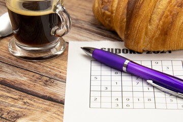 feuille de sudoku sur une table avec un café et croissant