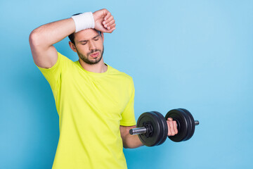 Photo of unhappy upset young man hold hand dumbbell heavy weak workout isolated on blue color background