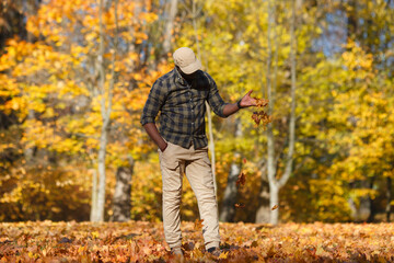 A cute black guy walks in an autumn park in golden foliage.