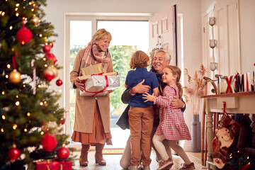 Grandchildren Greeting Grandparents As They Arrive With Presents To Celebrate Family Christmas