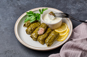 Traditional dolma with parsley and lemon in light plate with napkin on dark table, on black fork pricked piece of dolma over the saucepan