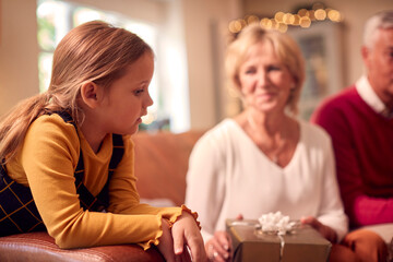 Granddaughter With Grandparents Opening Gifts Around Christmas Tree At Home