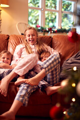 Obraz na płótnie Canvas Three Children Wearing Pyjamas Opening Gifts Around Christmas Tree At Home