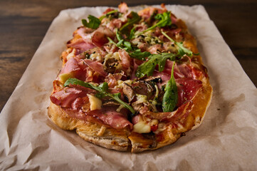 Close up rectangular Roman pizza with prosciutto ham, tomatoes, mozzarella, mushrooms and arugula
