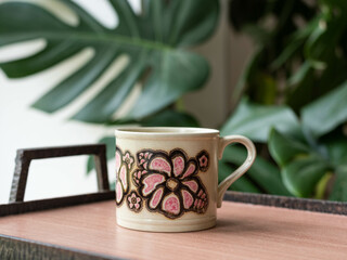Mid-century modern pottery, flower pattern mug on a wooden table with philodondendron in the background