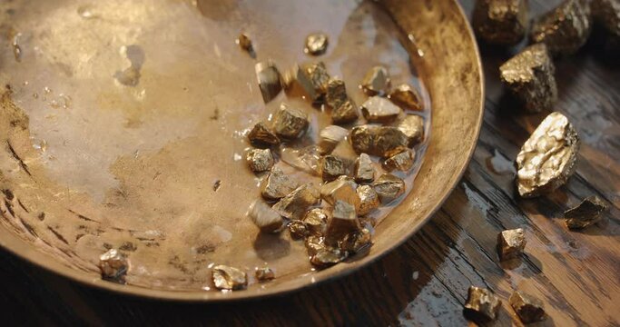 Gold nuggets slowly fall into a copper vintage gold digging bowl. Slow motion 150 fps 4K video. 