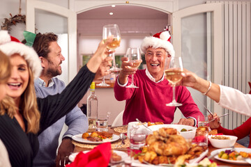 Multi Generation Family In Santa Hats Making Toast Whilst Eating Christmas Meal At Home Together