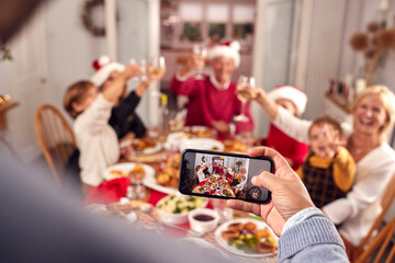POV Shot Of Person Taking Photo Of Multi-Generation Family Meal At Christmas On Mobile Phone
