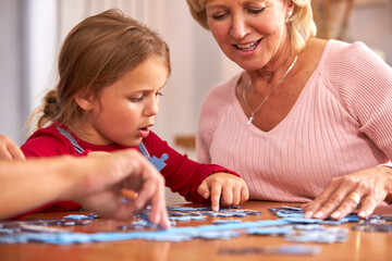 Granddaughter With Grandmother Sitting Around Table At Home Doing Jigsaw Puzzle Together
