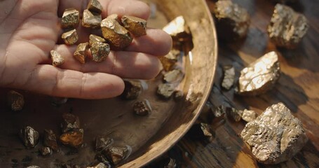 Gold nuggets slowly fall into a copper vintage gold digging bowl. Slow motion 150 fps 4K video. 