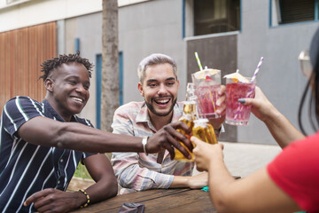 Happy friends having fun hanging out at outdoors terrace bar in the city - Young people enjoying and toasting beer and drinks to celebrate friendship