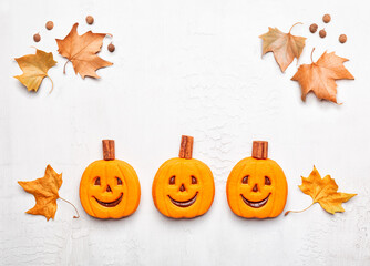 Happy Halloween background with funny smiling pumpkin cookies and autumn leaves. White surface.