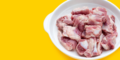 Raw pork ribs in white bowl on yellow background.