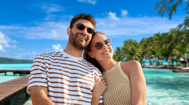 travel, tourism and people concept - happy couple in sunglasses over tropical beach background in french polynesia