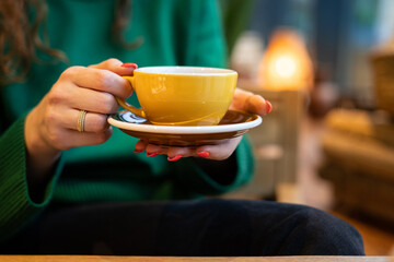yellow ceramic mug with saucer in female hands