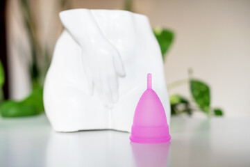 Menstrual cup on the background of a white vase statue in the form of a women's body. Woman's health, save planet and environmentally friendly feminine hygiene product concept, critical day