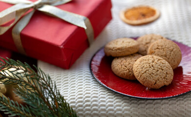 bake, food and winter holidays concept - close up of oatmeal cookies on red ceramic plate and christmas gift at home