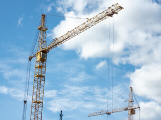 Construction concept. Tower cranes against a bright blue sky with clouds