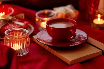 holidays, christmas and celebration concept - coffee in red ceramic cup with saucer and burning candles at home
