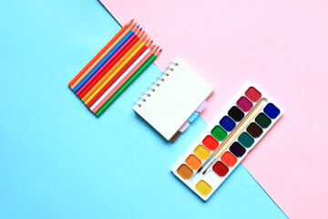 A set of paints and pencils for drawing on a pink background. Stationery for school. Layout of goods for the artist. View from above.