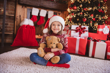 Photo of pretty charming school girl wear print pullover headwear smiling sitting floor hugging bear indoors house home room