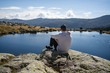 Fototapeta na wymiar A man with a lake and mountains in background. Location in Laguna Grande of Peñalara, in Madrid
