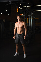 Fototapeta na wymiar shirtless muscular man in shorts and sneakers looking away while standing in gym.