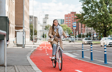 traffic, city transport and people concept - happy smiling woman riding bicycle along red bike lane...