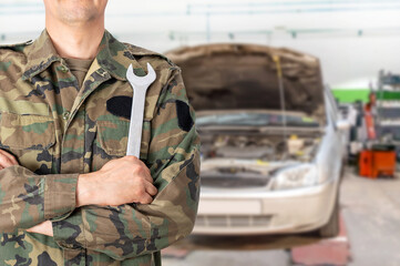 Hand of a military car mechanic with wrench. Car repair garage.